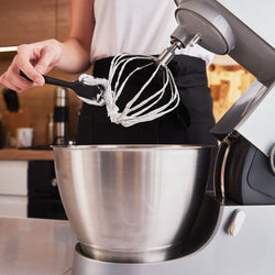 Person using a stand mixer with a whisk attachment in a kitchen setting.